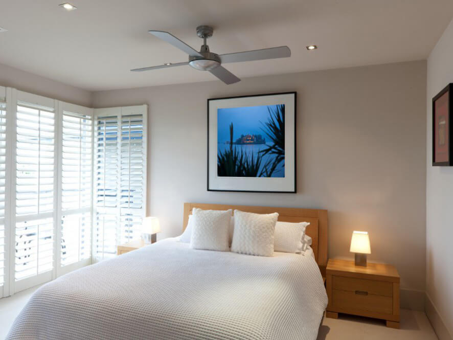 Neutral holiday home bedroom wooden bedhead and textured blanket with lamp and ceiling fan